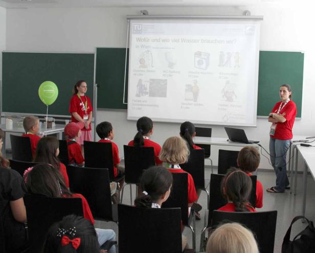 Kinder sitzen in einem Klassenzimmer und hören einem Vortrag über Wasserverbrauch zu.