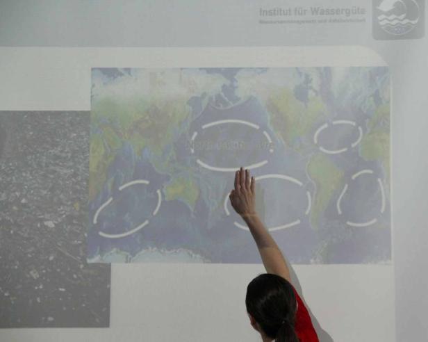 Eine Person zeigt auf eine Weltkarte mit eingezeichneten Meeresströmungen.