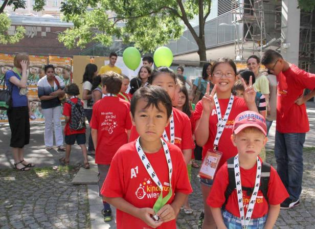 Eine Gruppe Kinder in roten T-Shirts der Kinderuni Wien steht im Freien.