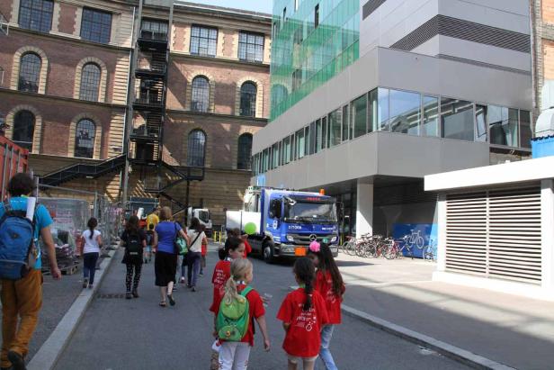 Eine Gruppe von Kindern geht an einem Lastwagen und modernen Gebäuden vorbei.