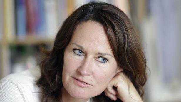 Eine Frau mit braunen Haaren und blauen Augen blickt nachdenklich zur Seite.