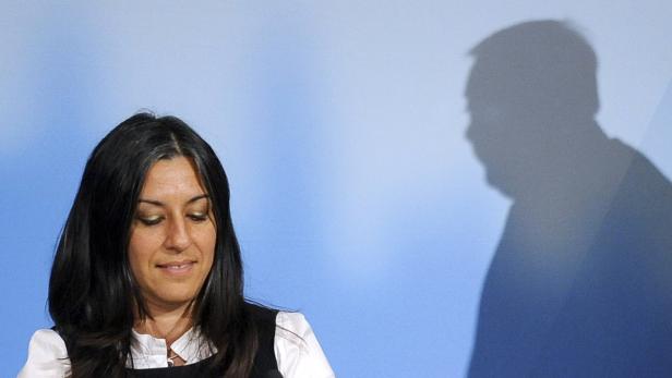 Eine Frau mit dunklen Haaren steht vor einer blauen Wand, auf der ein Schatten zu sehen ist.