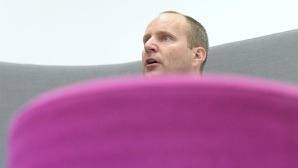 Ein Mann mit hellen Haaren spricht, während er in einem Sessel sitzt.