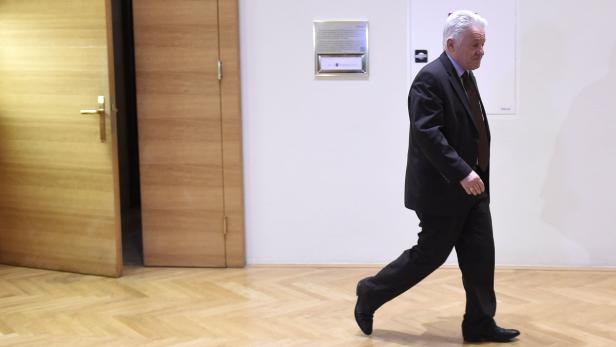 Ein Mann in einem dunklen Anzug geht in einem Flur entlang.