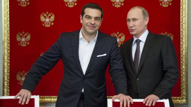 Alexis Tsipras und Wladimir Putin posieren vor einem roten Hintergrund mit goldenen Emblemen.