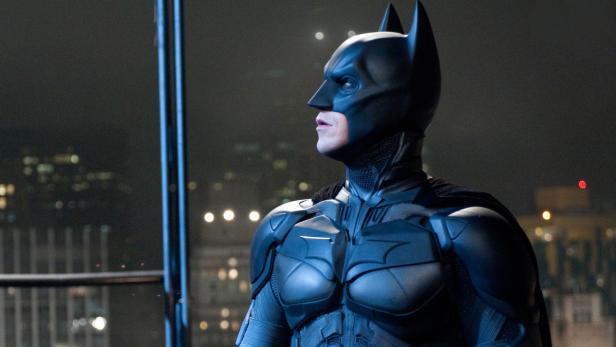 Batman steht in seinem Kostüm vor der Skyline von Gotham City.