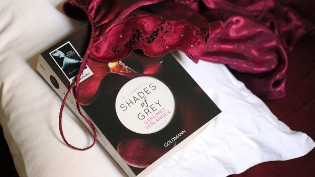 Das Buch „Shades of Grey“ liegt zusammen mit einem roten Negligé auf einem weißen Kissen.
