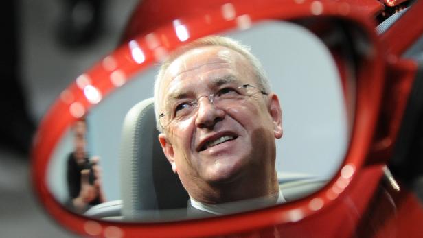 Ein Mann mit Brille sitzt in einem roten Auto und lächelt.