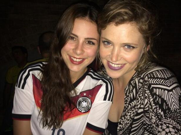 Zwei lächelnde Frauen, eine im Deutschland-Trikot, posieren für ein Foto.