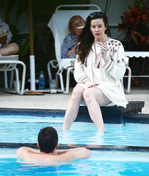 Liv Tyler sitzt am Poolrand und trinkt einen Drink.