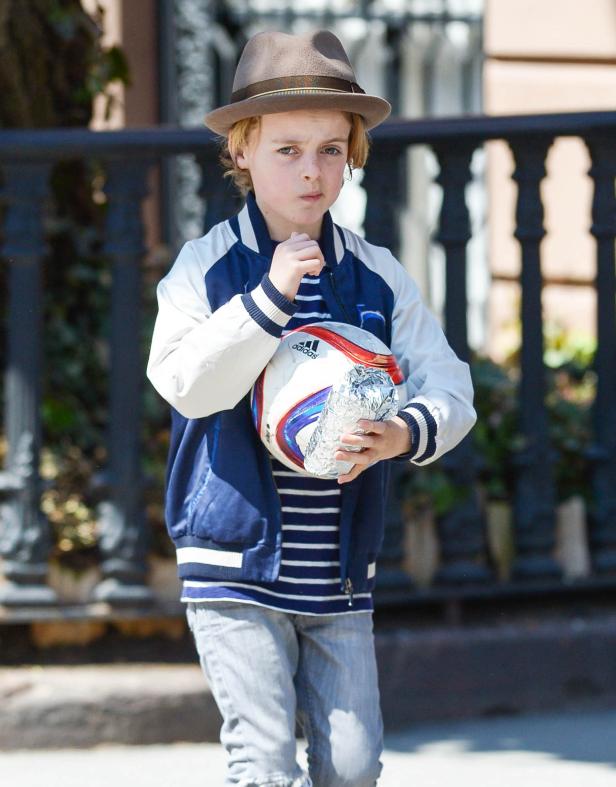 Ein Junge mit Hut hält einen Fußball und ein in Folie verpacktes Objekt.