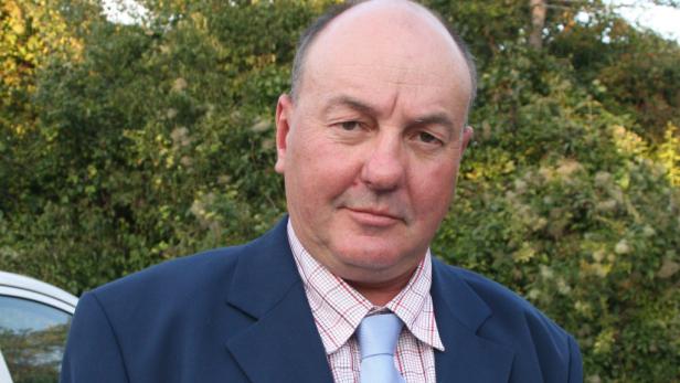 Ein Mann in Anzug und Krawatte vor einem grünen Hintergrund.