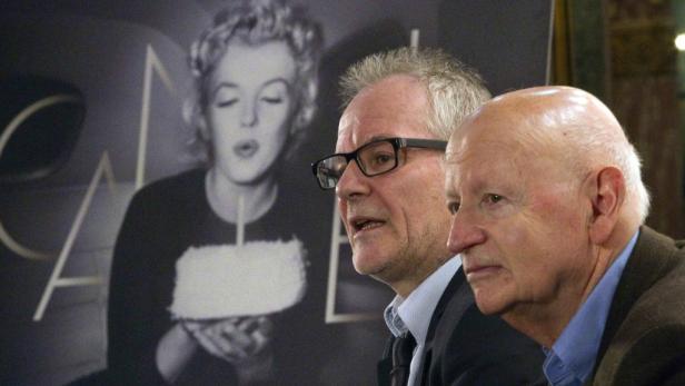 Zwei Männer stehen vor einem Porträt von Marilyn Monroe mit einer Geburtstagstorte.