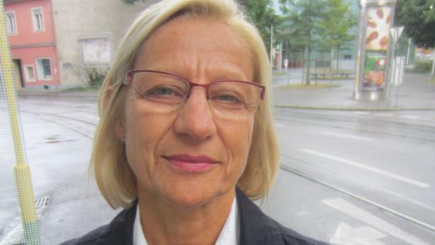 Eine Frau mit blonden Haaren und Brille steht auf einer Straße.