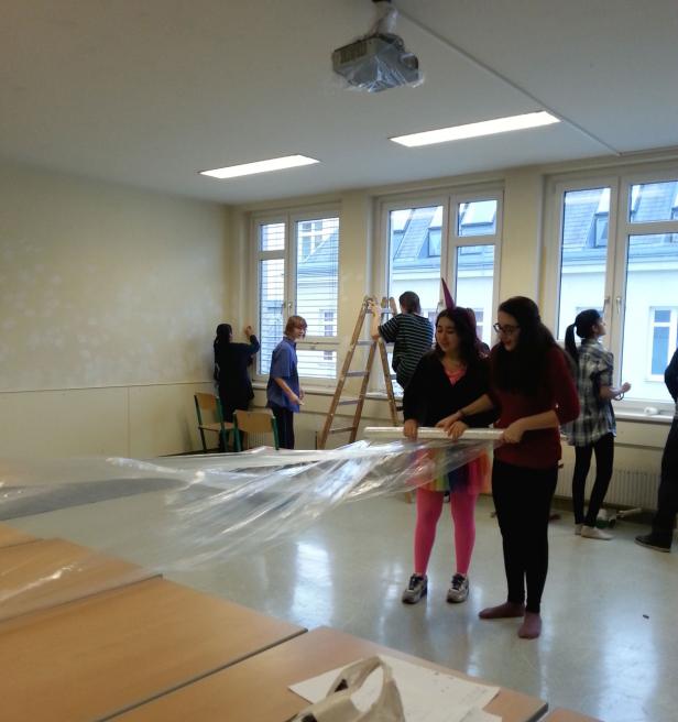 Schüler dekorieren einen Klassenraum mit Folie und einer Leiter.