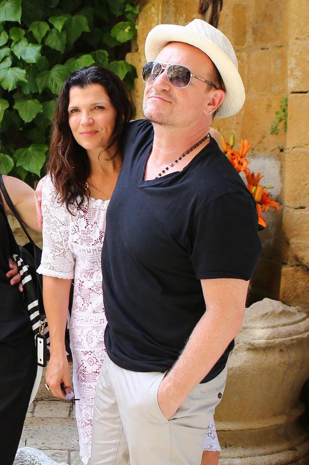 Bono posiert mit einer Frau vor einer Wand mit Pflanzen und Blumen.