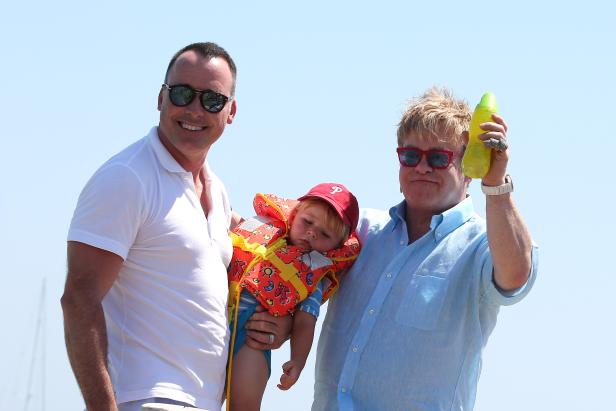 David Furnish und Elton John mit einem Kind in einer Schwimmweste.
