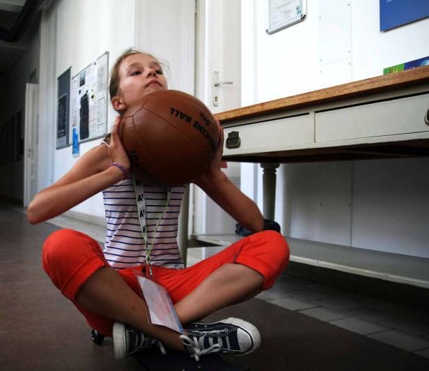 Ein Mädchen sitzt mit einem Medizinball im Arm auf dem Boden.