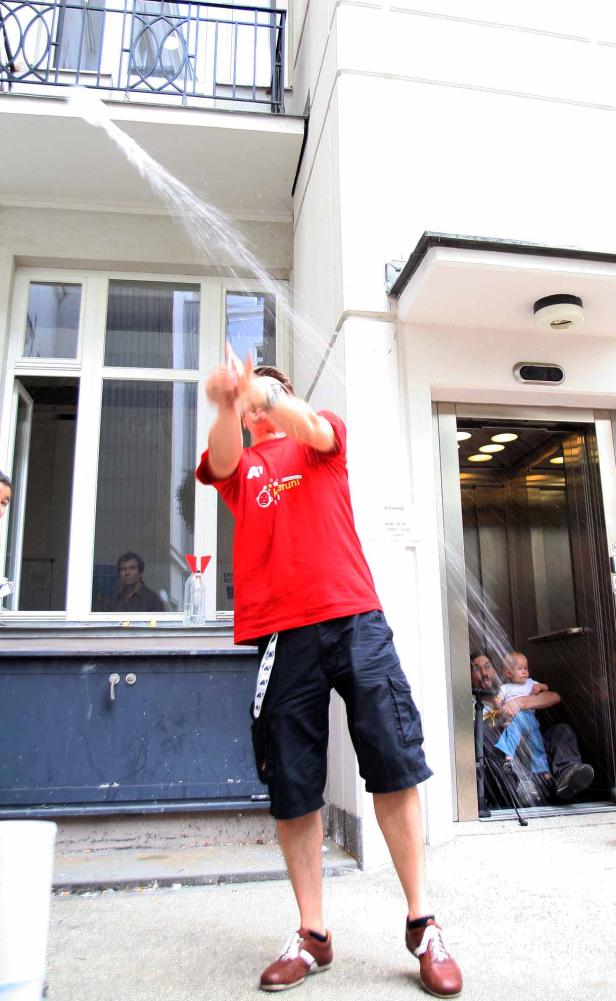 Ein Mann schüttet Wasser über eine Person mit Baby in einem Aufzug.