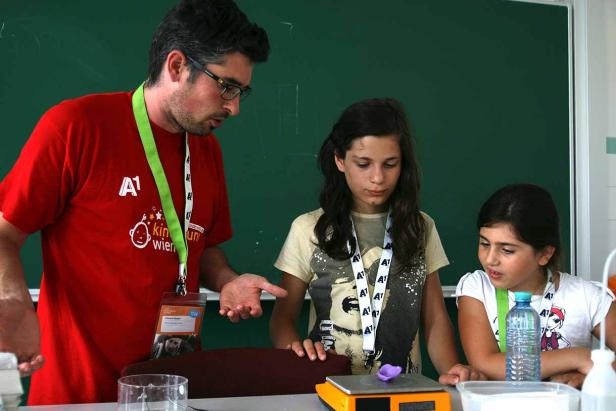 Ein Mann erklärt zwei Mädchen ein Experiment im Klassenzimmer.