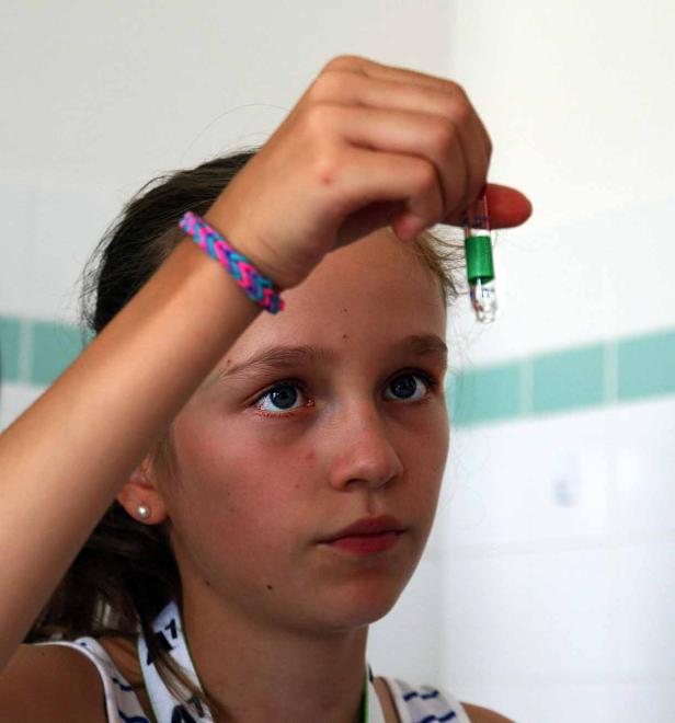 Ein junges Mädchen betrachtet eine kleine Ampulle mit einer grünen Flüssigkeit.