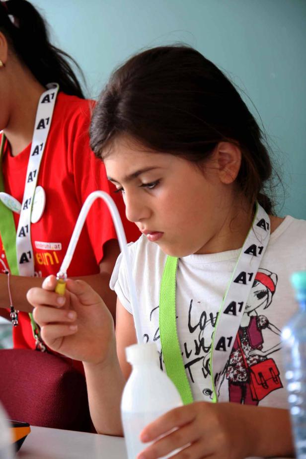 Ein Mädchen experimentiert mit einem Schlauch und einer Flasche Wasser.