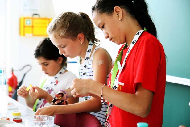 Drei Mädchen basteln gemeinsam an einem Tisch mit bunten Materialien.