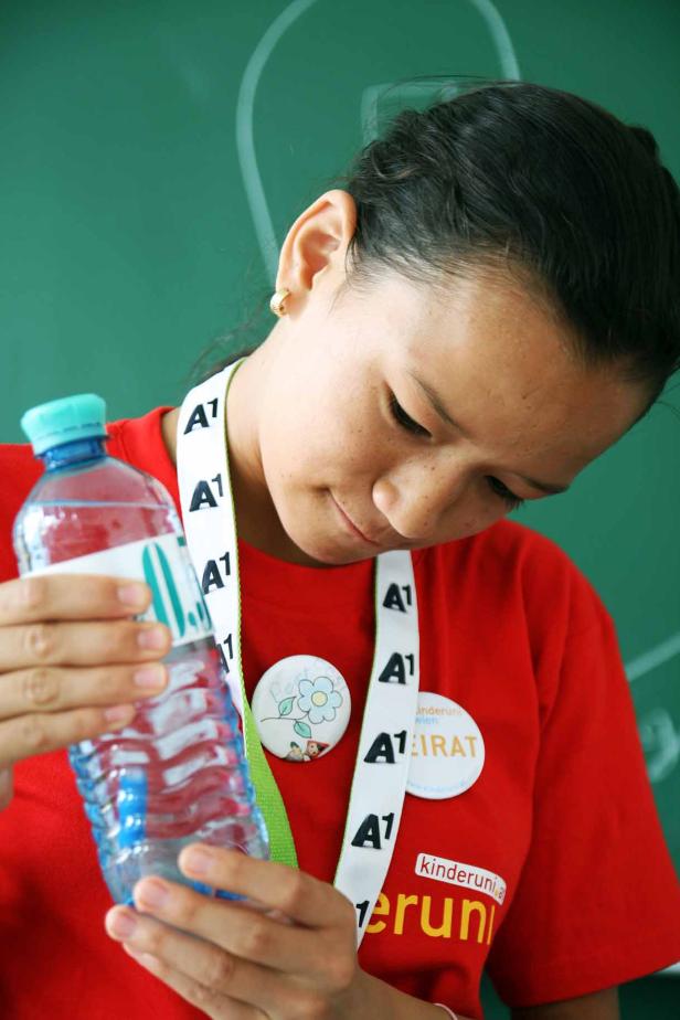 Ein junges Mädchen in einem roten T-Shirt betrachtet eine Wasserflasche.