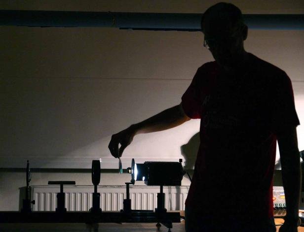 Eine Person manipuliert eine Linse in einem dunklen Raum mit optischen Geräten.