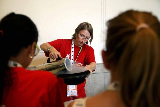 Eine Frau mit Brille gießt eine rauchende Flüssigkeit in einen Hut.