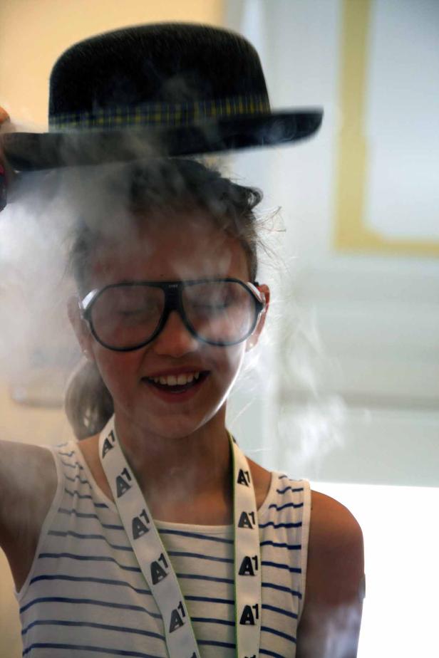 Ein Mädchen mit übergroßer Brille und Hut steht im Nebel.