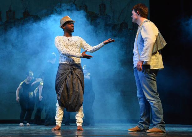 Auf einer Bühne stehen zwei Männer in Kostümen vor einer Gruppe von Tänzern.