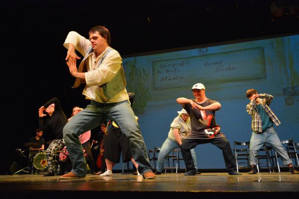 Eine Gruppe von Darstellern führt ein Theaterstück auf einer Bühne auf.