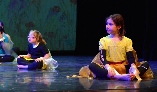 Zwei junge Tänzerinnen sitzen auf einer Bühne und bereiten sich auf ihren Auftritt vor.