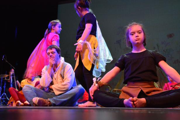 Eine Gruppe von Kindern und ein Mann sitzen auf einer Bühne während einer Aufführung.