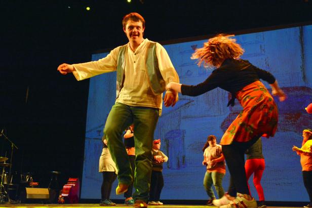 Auf einer Bühne tanzen ein Mann und eine Frau, während andere im Hintergrund stehen.