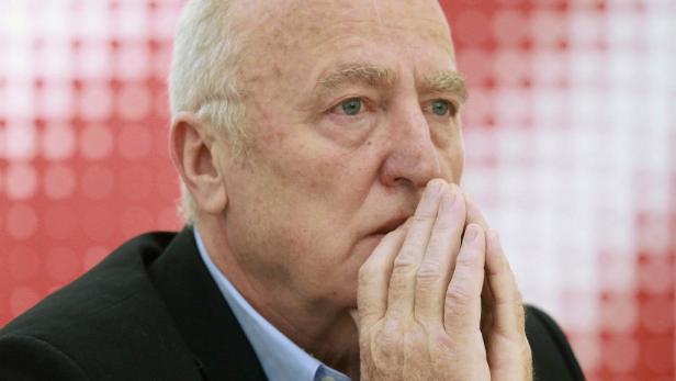 Ein Mann in einem Anzug hält seine Hände vor das Gesicht.