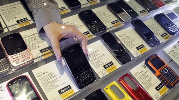 Eine Hand greift nach einem Nokia-Handy in einer Vitrine voller Mobiltelefone mit Preisschildern.