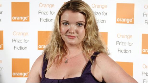 Eine Frau mit blonden, gewellten Haaren vor einem Hintergrund des „Orange Prize for Fiction“-Logos.