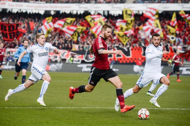 Fußballspieler kämpfen um den Ball vor einer Zuschauertribüne.