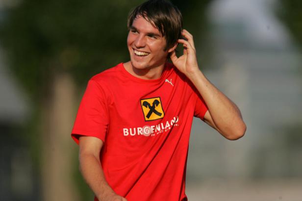 Ein lächelnder junger Mann in einem roten T-Shirt mit dem Aufdruck „Burgenland“.