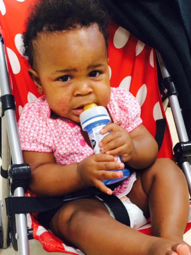 Ein Baby sitzt in einem rot-weiß gepunkteten Kinderwagen und hält eine Trinkflasche.