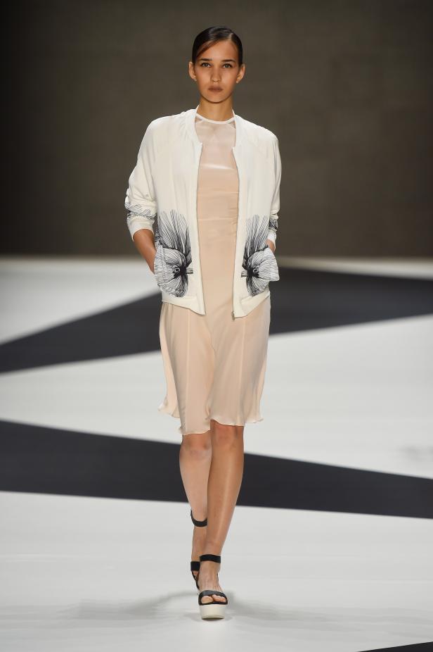 Eine Frau präsentiert ein Outfit mit einer weißen Jacke und einem hellen Kleid.