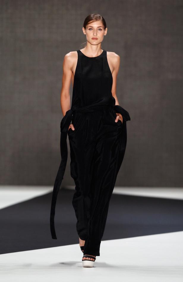 Eine Frau präsentiert einen schwarzen Hosenanzug auf einem Laufsteg.
