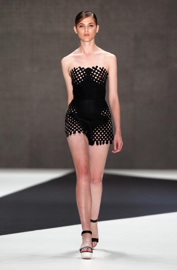 Eine Frau präsentiert ein schwarzes, ausgeschnittenes Ensemble auf einem Laufsteg.