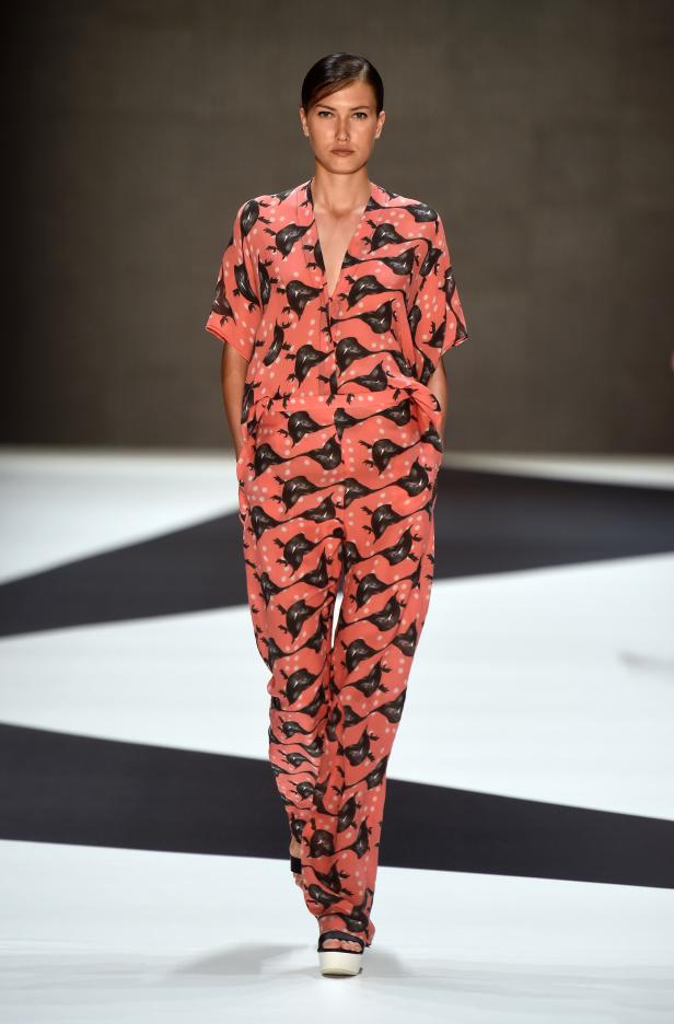 Eine Frau in einem korallenroten Pyjama-Anzug mit Vogelmuster auf einem Laufsteg.