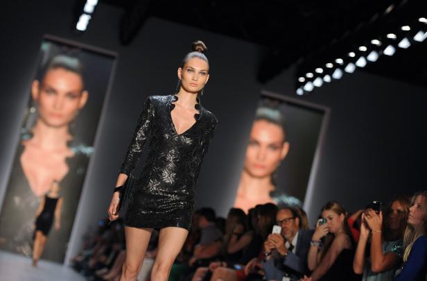 Eine Frau präsentiert ein kurzes, schwarzes Kleid auf einem Laufsteg.