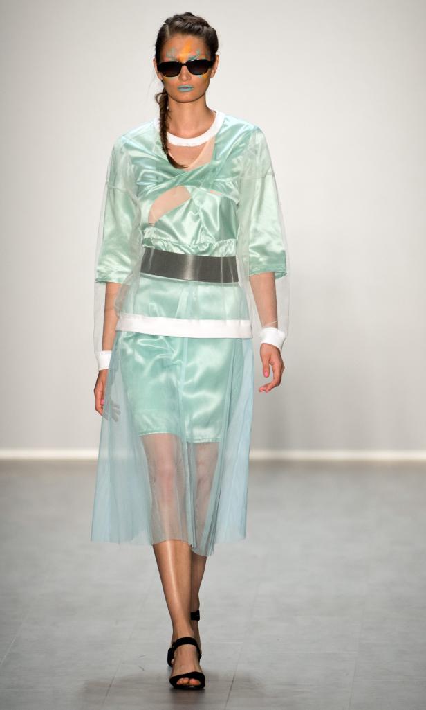 Eine Frau mit Sonnenbrille und Gesichtsbemalung trägt ein mintgrünes Kleid auf dem Laufsteg.