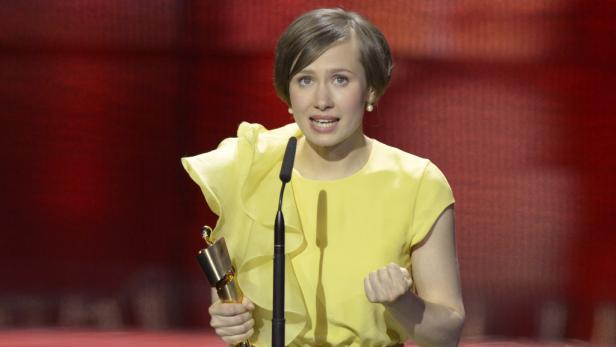 Beste Schauspielerin: Alina Levshin, für das Neonazi-Drama "Kriegerin" Eine Frau in einem gelben Kleid hält eine Auszeichnung und spricht in ein Mikrofon.