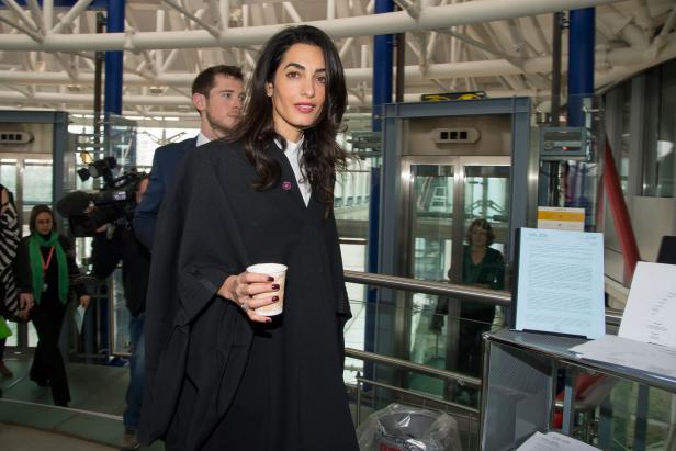Amal Clooney mit einem Kaffee in der Hand auf dem Weg durch ein Gebäude.
